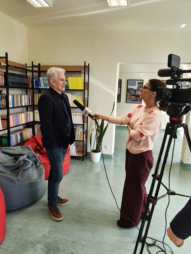 uczniowie siedący na krzesłach słuchają wypowiedzi mężczyzny, na środku pan z kamerą